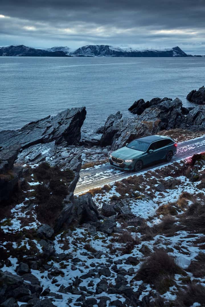 BMW i5 Touring eDrive parked near rocky shoreline.